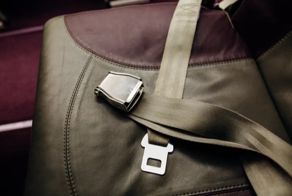Finished lap belt assembly with webbing, metal buckle and latch plate laid across a seat